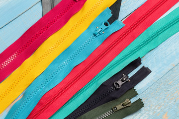 Pack lot of colorful plastic and metal zippers stripes with sliders pattern for handmade sewing tailoring on the blue denim background close up selective focus