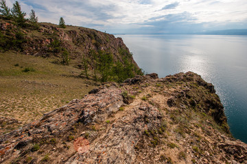 Fototapeta na wymiar The steep shore on Lake Baikal in cloudy weather.Coniferous trees grow. Mountains are visible across the lake.