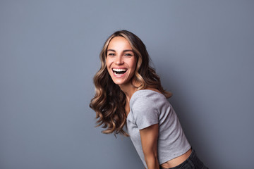 Portrait of beautiful young girl laughing on grey background.