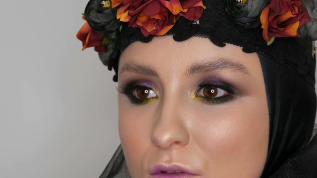 Professional girl model with beautiful makeup poses in a black cap and wreath on her head in front of the camera in the image of a black widow. High-fashion
