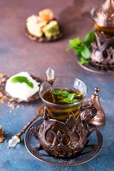 Traditional turkish tea with mint leaves and sweets in a traditional glass on a concrete background