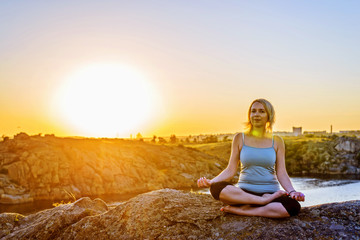 Young woman doing yoga on top of a mountain at sunset, free space.