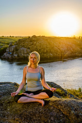 Young woman doing yoga on top of a mountain at sunset, free space.