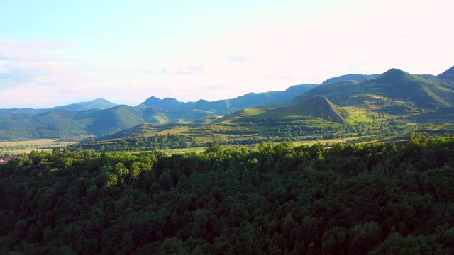 A long shot drone shot, rising up from the forest of the Coltesti mountain range, Romania. From the trees emerge a vast landscape of green mountains which stretch to the far corners of the shot.