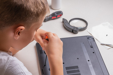 A boy of 10 years old is sorting a laptop for cleaning and maintenance. Selective focus. Screwdrivers, purge cylinder, magnifying glass and spray cleaner in the frame.