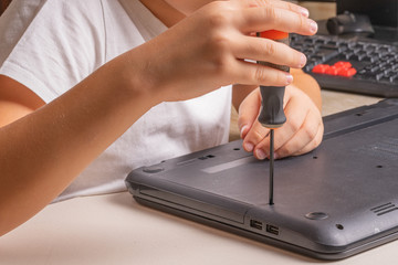 A boy of 10 years old is sorting a laptop for cleaning and maintenance. Selective focus. Screwdrivers, purge cylinder, magnifying glass and spray cleaner in the frame.
