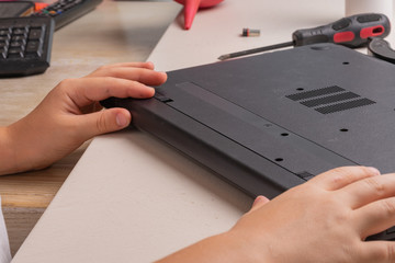 A boy of 10 years old is sorting a laptop for cleaning and maintenance. Selective focus. Screwdrivers, purge cylinder, magnifying glass and spray cleaner in the frame.
