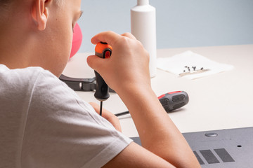 A boy of 10 years old is sorting a laptop for cleaning and maintenance. Selective focus. Screwdrivers, purge cylinder, magnifying glass and spray cleaner in the frame.