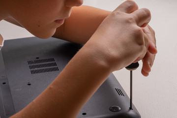 A boy of 10 years old is sorting a laptop for cleaning and maintenance. Selective focus. Screwdrivers, purge cylinder, magnifying glass and spray cleaner in the frame.