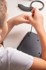 A boy of 10 years old is sorting a laptop for cleaning and maintenance. Selective focus. Screwdrivers, purge cylinder, magnifying glass and spray cleaner in the frame.