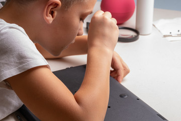 A boy of 10 years old is sorting a laptop for cleaning and maintenance. Selective focus. Screwdrivers, purge cylinder, magnifying glass and spray cleaner in the frame.