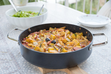 potato dish with sausages, bowl with salad defocused, dinner outdoors