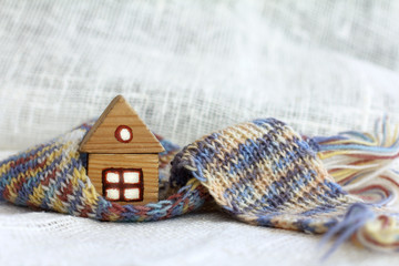 small wooden house with light in the windows is wrapped in a knitted scarf on a light background. insulated outside cozy inside