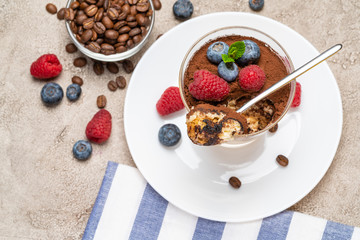 Classic tiramisu dessert portion with blueberries and raspberries in a glass cup on concrete background