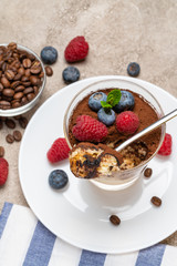 Classic tiramisu dessert portion with blueberries and raspberries in a glass cup on concrete background