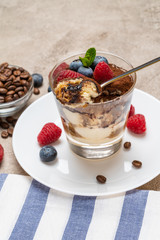 Classic tiramisu dessert portion with blueberries and raspberries in a glass cup on concrete background
