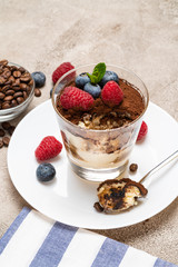 Classic tiramisu dessert portion with blueberries and raspberries in a glass cup on concrete background