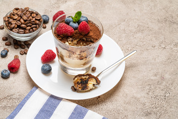 Classic tiramisu dessert portion with blueberries and raspberries in a glass cup on concrete background