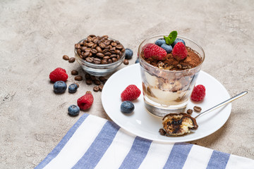 Classic tiramisu dessert portion with blueberries and raspberries in a glass cup on concrete background