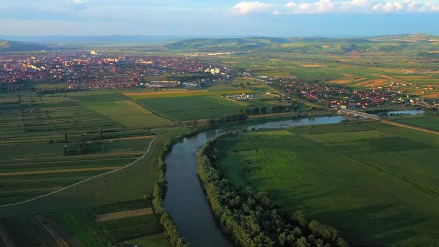Mures river passing through green area with small town on its left bank, aerial view