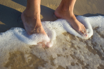 Fototapeta premium Feet young man on sand sunrise background sea, beach wave
