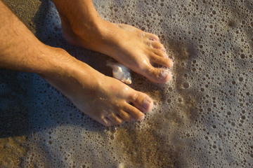 Feet young man on sand sunrise background sea, beach wave seashells