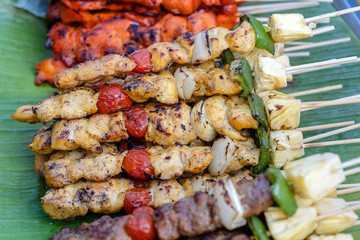 Skewers with pieces of grilled barbecue, green bell pepper, red tomato and meat for sell in street market, Thailand, closeup