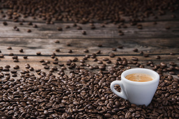 White cup of coffee espresso with beans on brown wooden table