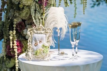 Wedding composition: arch of flowers, table, champagne glasses, pen, solemn frame with gold wedding rings.