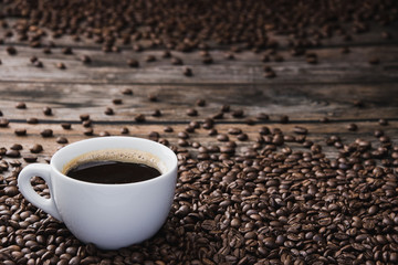White cup of coffee with beans on brown wooden table