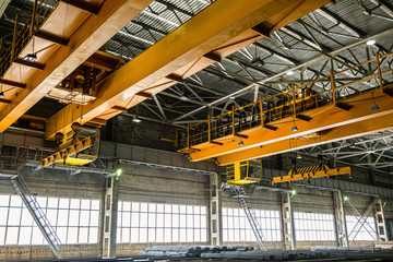 Two yellow overhead cranes in engineering plant shop. Industrial metalwork production hall and warehousing workshop.