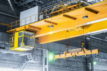 Yellow overhead crane with linear traverse and hooks in engineering plant shop. Cabin of crane...