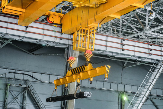 Yellow overhead crane carries cargo in engineering plant shop. Jib crab trolley with hooks and linear traverse.
