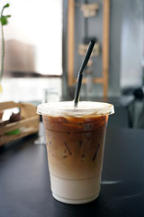 Iced Latte - A plastic glass of coffee with fresh milk and vanilla syrup on table and blurred background, Perfect drink for summer time.