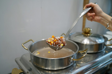 Homemade Soft Boiled Rice (Rice Porridge) with grains - Hand using dipper to ladle congee from hot pot, Traditional Chinese food style and Popular street food in Thailand.