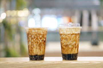 Bubble Milk Tea - Two plastic glasses of fresh milk with black sugar syrup (Kuromitsu) and hot black pearl (Boba) topped with cream cheese on blurred background, Taiwanese drinking culture.