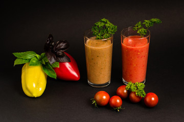 Still life. Vegetable juices in glass glasses, tomatoes, yellow pepper, green and purple basel leaves, parsley on a black background. Close-up. Isolated. Vegetarianism.