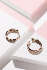 Detail close-up shot of a pair of patchy congo earrings with golden fasteners. The hoop earrings...