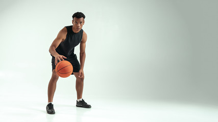 Obraz premium Ready to win. Full length of young african man in sports clothing playing basketball in studio against grey background