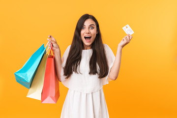 Portrait of delighted shopaholic woman wearing dress holding credit card and colorful shopping bags