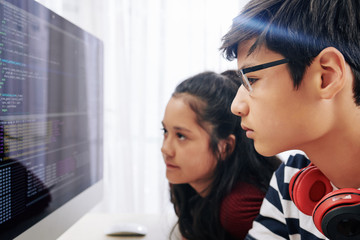 Serious pensive teenagers examining programming code on screen of computer and searching for mictake