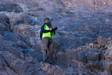 Obraz premium A bearded man on the mountain of Moses with a camera, pilgrimage to the holy places. Nature photographer taking photos in the mountains.