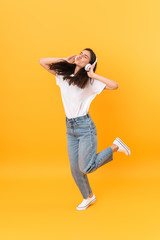 Image of excited brunette woman with long hair smiling while listening to music with headphones