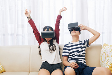 Brother and sister sitting on sofa at home and testing new video game for virtual reality headset