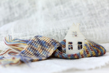 small wooden house with a pipe wrapped in a scarf on a background of light fabric. warming technology in the winter season