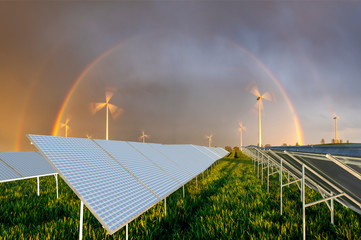 beautiful rainbow over a windmill farm and solar panels on a green field - clean renewable energy...