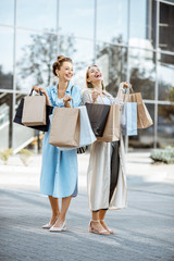 Two happy girlfriends feeling excited with purchases, standing together with shopping bags in front...