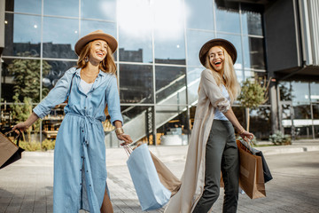 Portrait of two joyful and happy woman with shopping bags in front of the shopping mall, feeling excited with new purchases