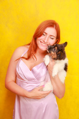 Relaxed red-haired girl embracing puppy on yellow background. Studio portrait of white appealing woman chilling with dog.