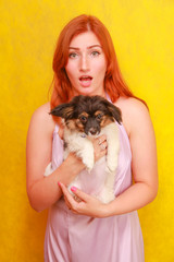 Fototapeta na wymiar Relaxed red-haired girl embracing puppy on yellow background. Studio portrait of white appealing woman chilling with dog.